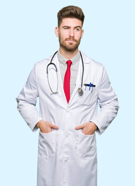 Young handsome doctor man wearing medical coat smiling looking side and staring away thinking. - Foto, Bild