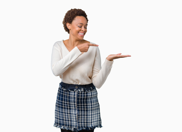 Młoda African American kobieta na białym tle zdumiony i uśmiechnięty do aparatu podczas prezentacji z ręki i wskazując palcem. - Zdjęcie, obraz