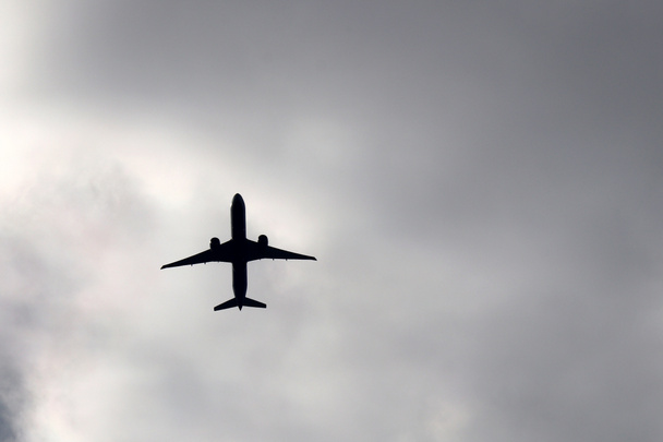 Repülő repülőgép viharfelhők háttérben. Sziluettje egy utasszállító repülőgép a sötét drámai égen - Fotó, kép