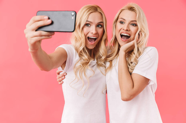 Surprised happy blonde twins wearing in t-shirts making selfie - Fotó, kép