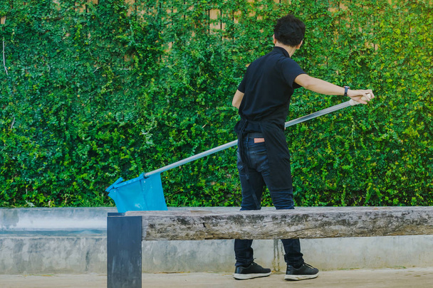 Junger Mann reinigt Brunnenbecken mit Netz von herabfallendem Laub  - Foto, Bild