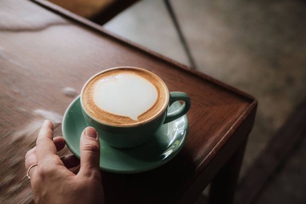 Woman hand holding coffee with heart latte art - Fotó, kép
