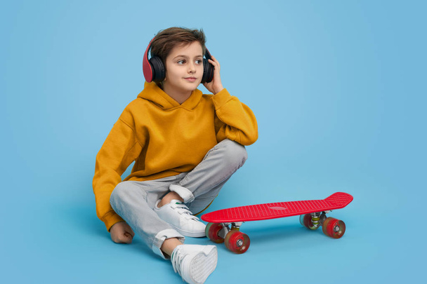 Stylish boy listening to music near skateboard - Foto, Imagem