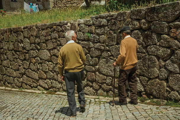Old people walking down the alley on slope next to stone wall - Foto, afbeelding