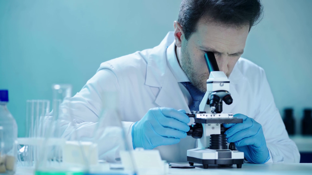 guapo científico haciendo investigación con microscopio y anotando resultados en laboratorio médico
 - Imágenes, Vídeo