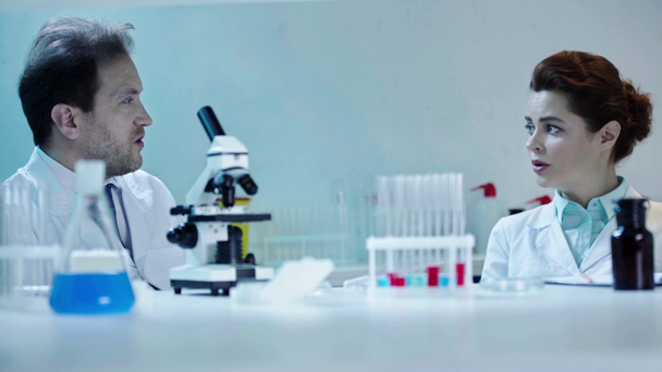 dois cientistas sérios falando em laboratório perto da mesa com vidraria médica
  - Filmagem, Vídeo