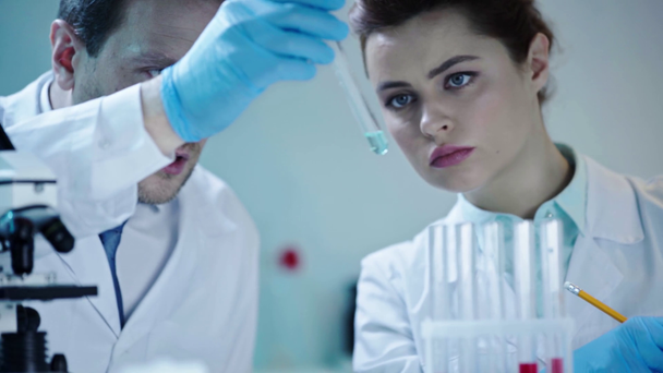 hübsche Ärztin schreibt mit Bleistift, während hübsche Wissenschaftlerin Reagenzglas mit Flüssigkeit in der Hand hält  - Filmmaterial, Video