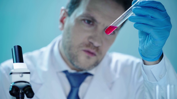 臨床検査室で赤い液体を持つ試験管を見ている深刻な科学者 - 映像、動画