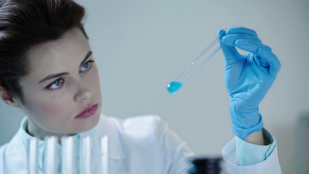 piękny naukowiec patrząc na niebieską ciecz w probówce w laboratorium klinicznym - Materiał filmowy, wideo