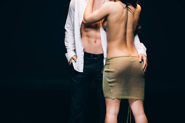 黒で孤立した裸の胴でエレガントなボーイフレンドの近くに立っているセクシーなお尻を持つ裸の女性の背面図 - 写真・画像