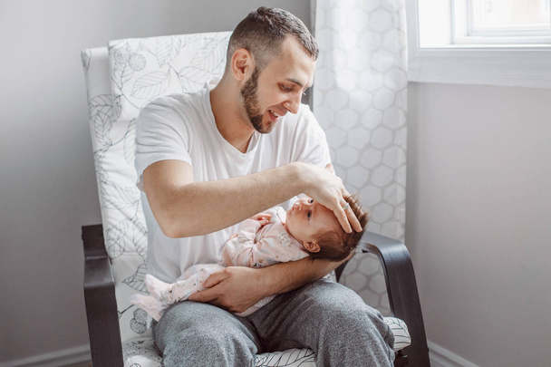 Caucasian father sitting in armchair with newborn baby girl. Parent holding rocking child daughter son on his hands. Authentic lifestyle documentary moment. Single dad family life concept. - Photo, Image