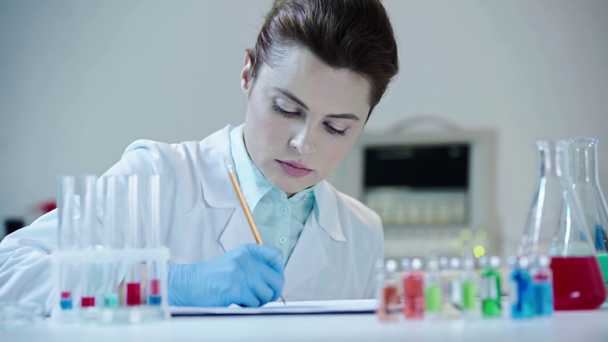 προσεκτικός επιστήμονας κοιτάζοντας διαφανές υγρό στο δοκιμαστικό σωλήνα και γράφοντας τα αποτελέσματα στο εργαστήριο - Πλάνα, βίντεο