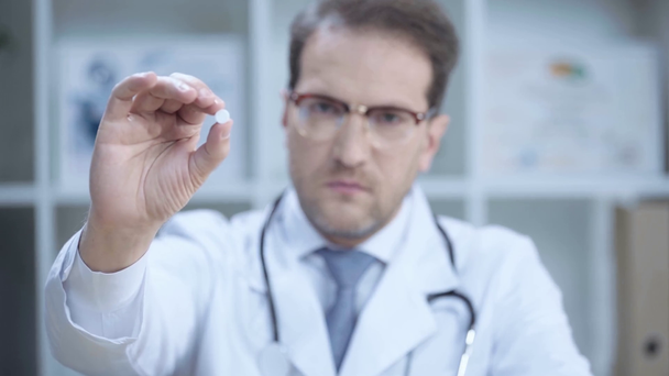 sebevědomý doktor v bílém plášti a brýlích s pilulkou a s pohledem na fotoaparát  - Záběry, video