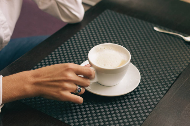 Mujer con hermosas manos está bebiendo café en la cafetería. Cappuccino de cerca en taza blanca, imagen con efecto de película y procesamiento de autor
. - Foto, Imagen