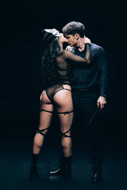сексуальная молодая женщина в костюме bdsm женщина рядом с мужчиной с поркой весло изолированы на черном
 - Фото, изображение