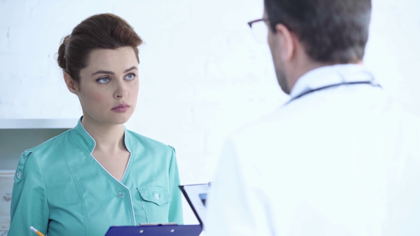 πίσω άποψη του γιατρού που μιλάει με όμορφη νοσοκόμα στέκεται κοντά και γράφοντας διάγνωση - Πλάνα, βίντεο