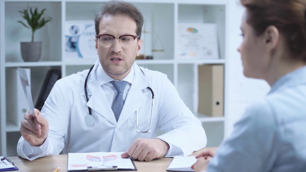 selectieve focus van serieuze arts zittend op werkplek, kijken naar x-ray diagnose en praten met assistent  - Video