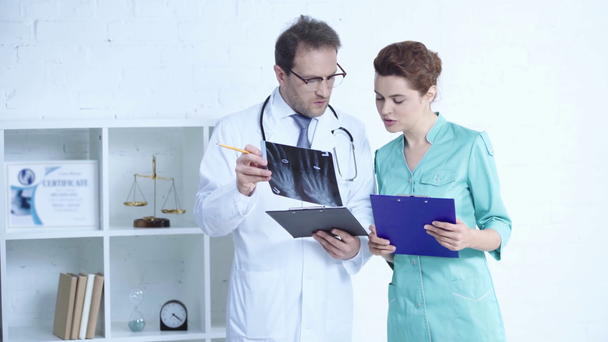 handsome doctor and pretty nurse standing with clipboards and talking while looking at x-ray diagnosis  - Footage, Video