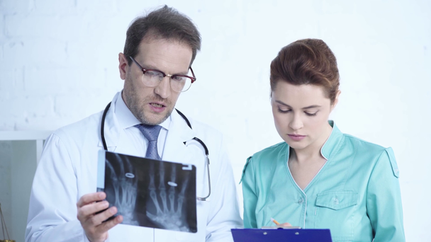 pretty nurse looking at x-ray diagnosis together with serious doctor and writing on clipboard - Footage, Video