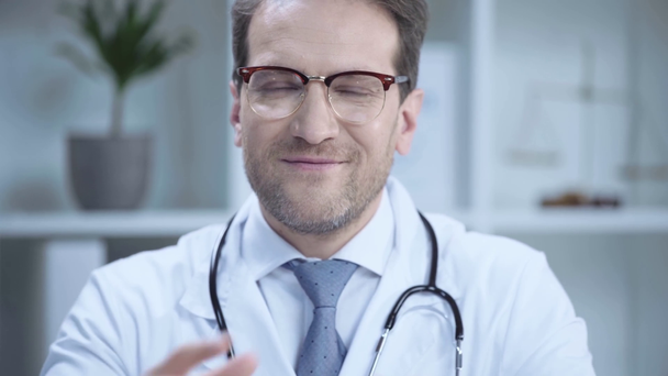 médico bonito em óculos adiando máscara médica, sorrindo e olhando para a câmera
 - Filmagem, Vídeo