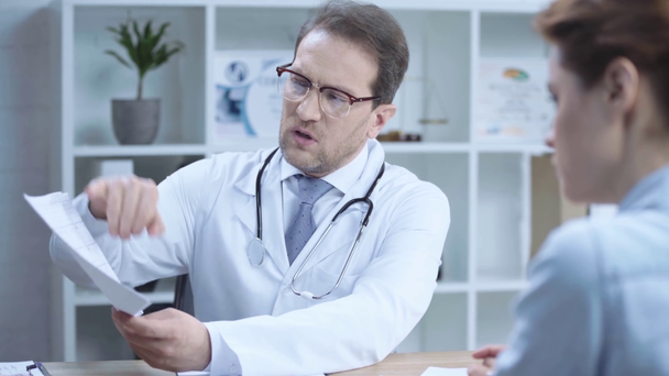 handsome doctor holding cardiogram while talking with colleague in hospital - Metraje, vídeo