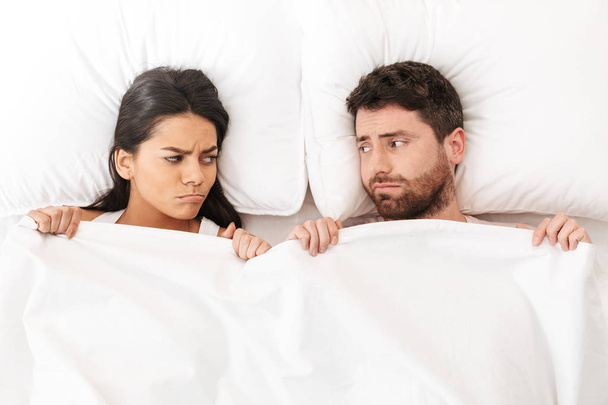 Displeased quarrel young loving couple lies in bed under blanket. - 写真・画像