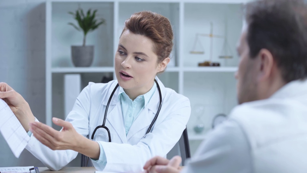 selektywne skupienie się na atrakcyjnym lekarza trzymający kardiogram i rozmawianie z kolegą - Materiał filmowy, wideo