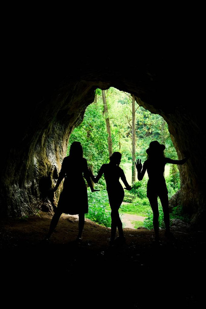 Dark female silhouettes at the entrance to natural cave in the forrest. - Foto, Imagem
