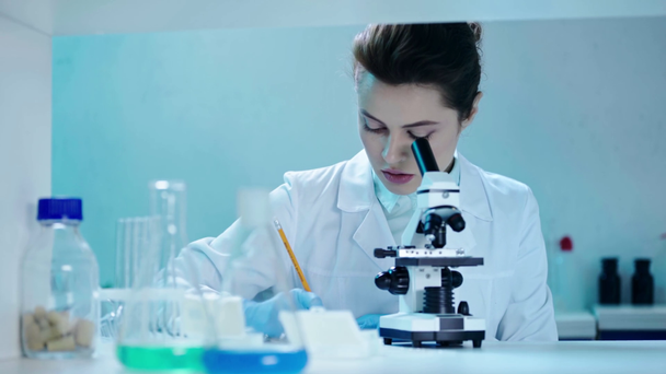 όμορφη, συγκεντρωμένη επιστήμονας κάνοντας ανάλυση με μικροσκόπιο σε κλινικό εργαστήριο - Πλάνα, βίντεο