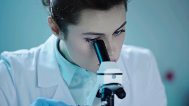 όμορφη, προσεκτική επιστήμονας κοιτάζοντας στο μικροσκόπιο, ενώ εργάζονται σε εργαστηριακές - Πλάνα, βίντεο