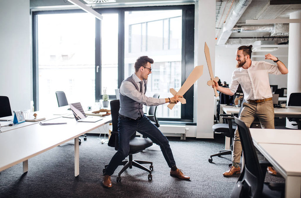 Two young businessmen with swords in an office, having fun. A competition concept. - Foto, Imagem