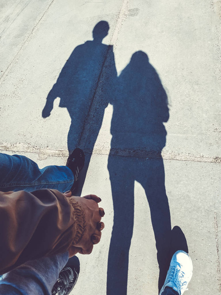 Sziluettjét egy pár szerelmes kéz a kézben jár öntés street hosszú árnyék a szerelem. Séta a gyalogosok a járdán tervezett árnyékában. Művészi fotó fekete-fehér, B&W, napsütéses napon - Fotó, kép