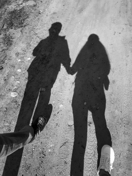 Silhouette di una coppia amore nel gettare mano nella mano amore su una lunga ombra sulla strada.Ombre di pedoni a piedi proiettati sul marciapiede. Foto artistica in bianco e nero, B & W nella giornata di sole
 - Foto, immagini