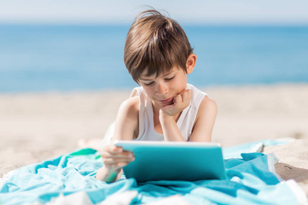 Garçon avec tablette couché sur la plage une journée ensoleillée
 - Photo, image