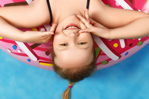 Zbliżenie Cute Little Girl w strój kąpielowy leżącego na pączek nadmuchiwane koło. Baby do góry nogami. Koncepcja lato. Niebieskie tło - Zdjęcie, obraz