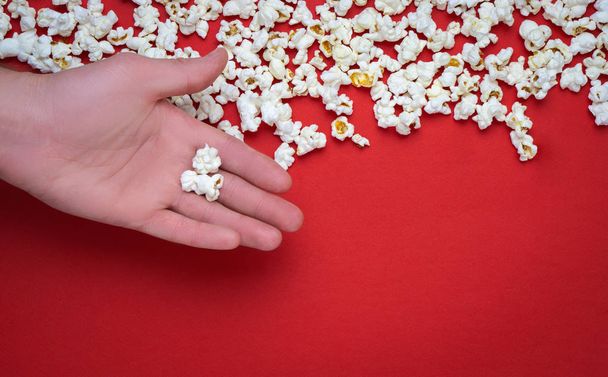 white popcorn on a red background.  hand holding Pop corn - Фото, изображение