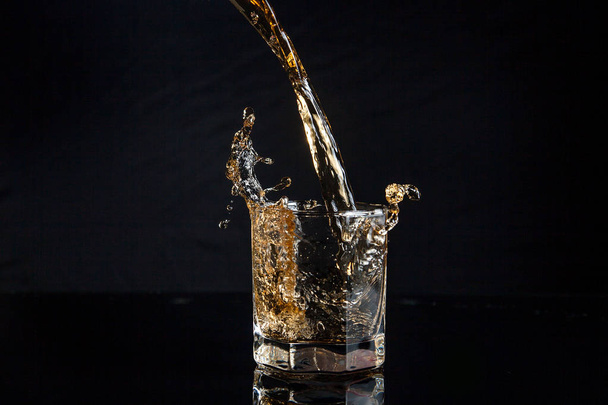 Whiskey pouring into glass with ice isolated on black background - Фото, изображение