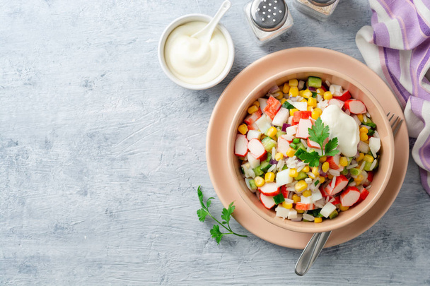Salad with crab sticks, sweet corn, cucumbers, boiled eggs, onion and rice in bowl on concrete background. Russian cuisine. Top view. Copy space. - Foto, Bild