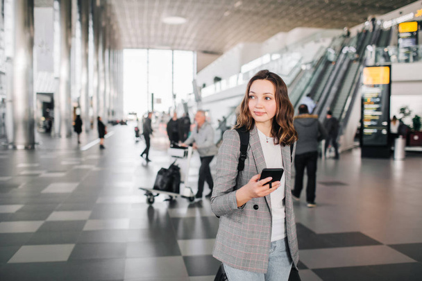 Girl at the airport, walking with her smartphone and baggage. - Фото, изображение