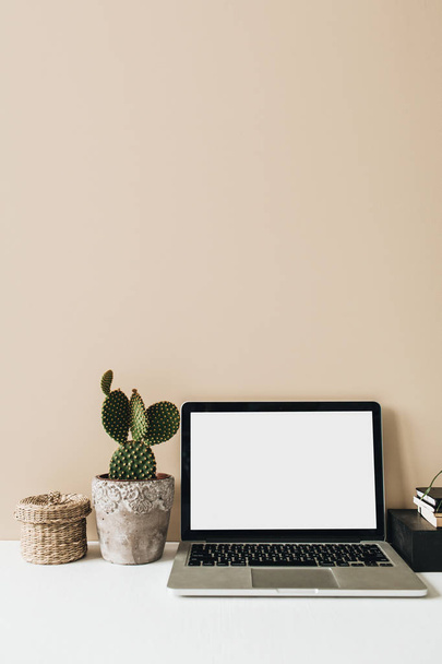 minimalistischer Homeoffice-Schreibtisch mit Laptop, Kaktus auf beigem Hintergrund. Kopierraum-Leerzeichen-Attrappe von vorne. Vorlage für Freiberufler. - Foto, Bild