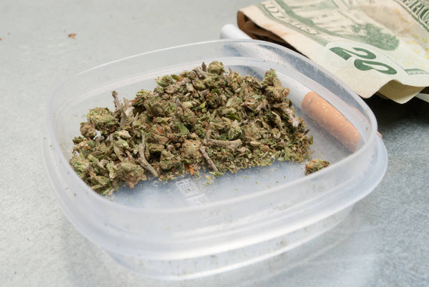 Close up view of dried marijuana in plastic container and money. Drug addiction concept. Medical marijuana concept  - Photo, Image