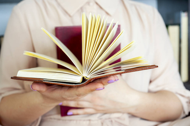 Ένα κορίτσι με ελαφρύ φόρεμα διαβάζει ένα βιβλίο. Τα γυναικεία χέρια κρατούν ένα βιβλίο στα χέρια τους. - Φωτογραφία, εικόνα