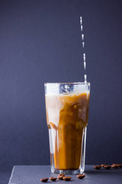 Iced coffee with milk on a dark background. Summer drink with caffeine on the slate board. Latte in a glass cup and coffee beans. Copy space - Photo, image