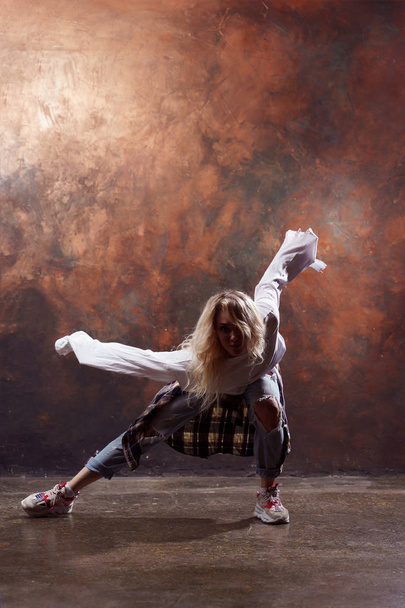 Photo of long-haired blonde woman in ripped jeans dancing on brown background - Valokuva, kuva