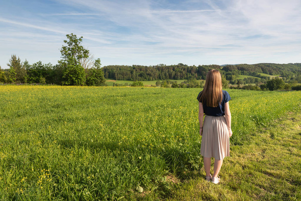 Молодая женщина с длинными волосами наслаждается красотой и ароматом весенних полей
. - Фото, изображение