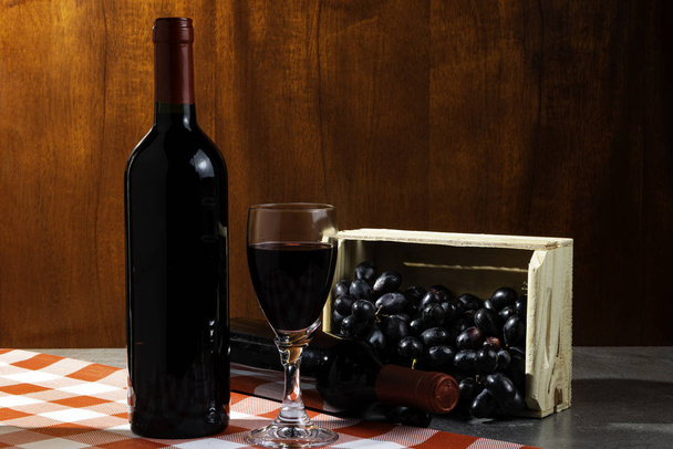 Bottle of red wine in wine cellar for tasting. Red wooden background with wooden box with grapes. Wine tradition and culture concept. - Photo, Image