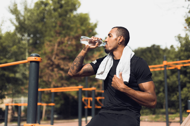 Спортивный человек пьет воду после тренировки на спортивной площадке
 - Фото, изображение