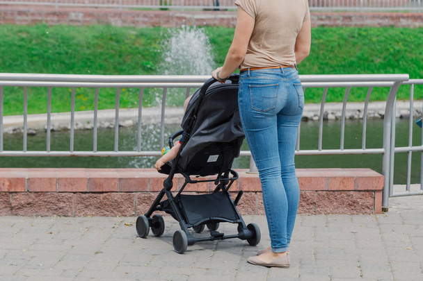 Beautiful woman with a child in a pram walks through a summer park. - Photo, Image