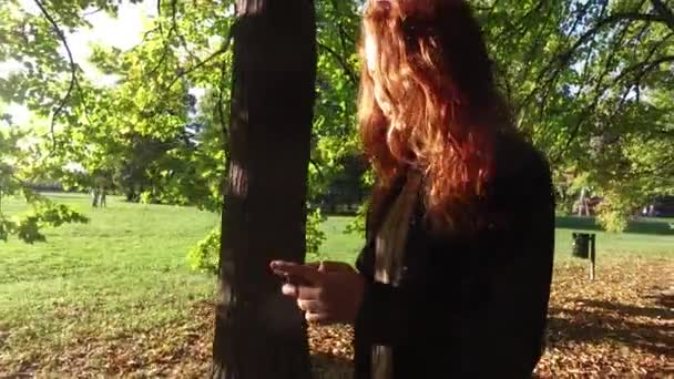Νεαρή γυναίκα που περπατάει σε εξωτερικούς χώρους στο ηλιόλουστο πάρκο - Πλάνα, βίντεο