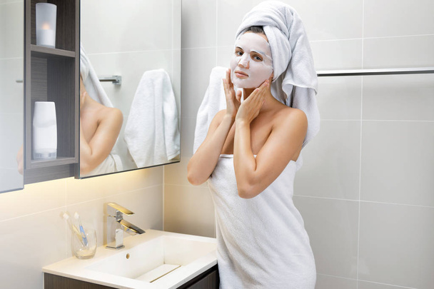 Woman in bathroom is applying facial sheet mask - Zdjęcie, obraz